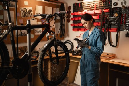 Young cute woman repair bicycle with mobile phone search spare parts on the internet in garage workshop. diy concept. Copy space