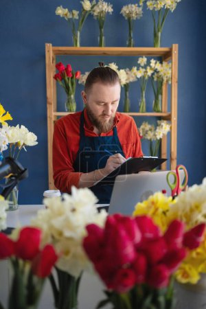 Small business owner florist working with laptop and clipboard in his flower shop. concept of own business. Copy space