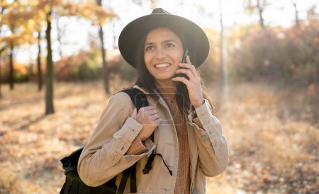 Mujer hispana hablando por teléfono mientras camina en un parque de otoño. Copiar espacio