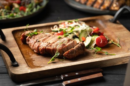 Beef steak cut into pieces served with fresh vegetables on a wooden board. Copy space
