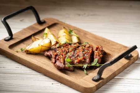 Foto de Filete de carne a la parrilla rebanado Ribeye medio raro que sirve en una tabla de servir de madera con papas en la mesa. Copiar espacio - Imagen libre de derechos