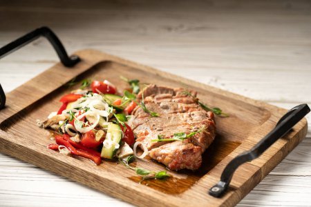 Steak de porc coupé en tranches servi avec des légumes sur une planche de bois sur une table blanche. Espace de copie