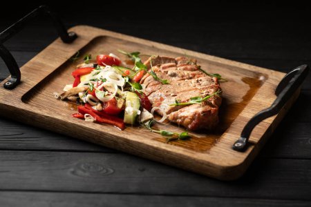 Steak de porc coupé en tranches servies avec des légumes sur une planche de bois sur un fond noir. Espace de copie