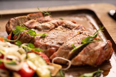 Close-up of beef and pork steak with fresh vegetables on a wooden board. Macro shot