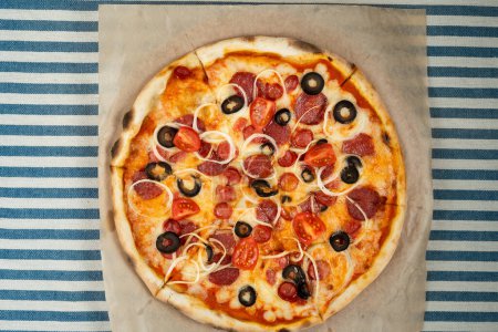 Top view of pizza with pepperoni, olives and tomato slices on craft paper on the table. Copy space