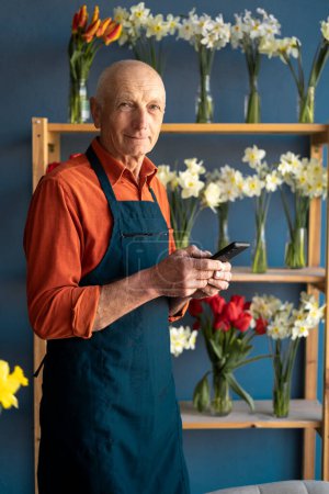 Un anciano, vendedor de flores, sosteniendo el teléfono con una sonrisa en la cara. Respuestas a SMS de los clientes