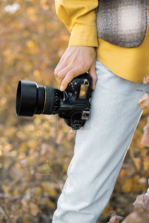 Téléchargez les photos : Gros plan d'une main tenant un appareil photo professionnel. Une jeune femme se tient dans la forêt d'automne. - en image libre de droit