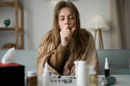 joven enferma mujer molesta sentada en el sofá en casa cubierta con una manta tosiendo intensamente, chica enferma con síntomas de gripe,