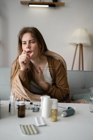 jeune femme malade bouleversée assise sur le canapé à la maison couverte d'une couverture toussant intensément, fille malade avec des symptômes de grippe. espace de copie.