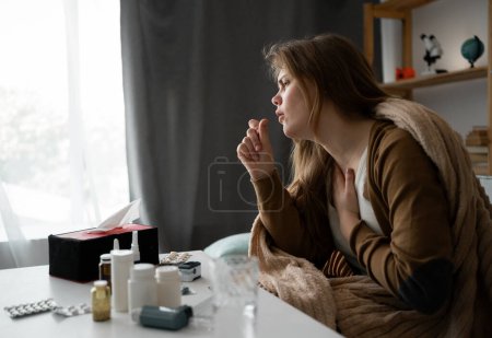 vue latérale. jeune femme malade bouleversée assise sur le canapé à la maison couverte d'une couverture toussant intensément, fille malade avec des symptômes de grippe. espace de copie. bannière