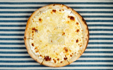 4 cheese pizza on a striped tablecloth lying on the table in an Italian pizzeria. Homemade baking and dough concept. Top view. Copy space