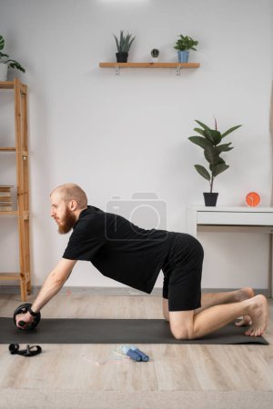 Handsome bearded man doing exercise with abs wheel on mat. Athletic man doing fitness workout at home. Bodybuilding, fitness workout concept. Copy space