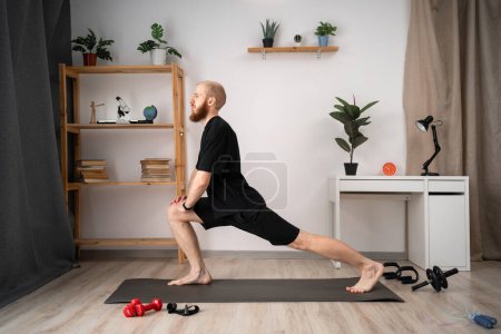 Athletic man doing forward lunge exercises at home in his apartment with cozy Interior. copy space