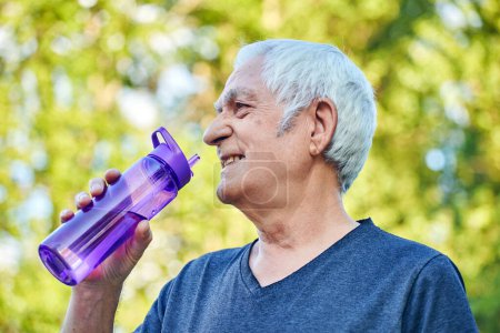 Photo for Mature man holds plastic reusable bottle drinking still mineral water during morning work out or stroll in summer park, caring about health, relieving thirst - Royalty Free Image