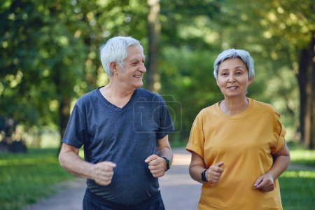 Téléchargez les photos : Mature fit couple jogging dans le parc d'été. Deux joggeurs plus âgés aiment le cardio actif matinal à l'extérieur, garder un mode de vie sain et actif. Perte de poids, concept sportif - en image libre de droit