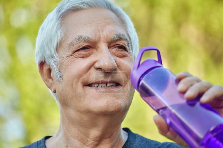 Photo for Close up face attractive mature man holds plastic reusable bottle drinking still mineral water during morning work out or stroll in summer park, caring about health, relieving thirst - Royalty Free Image