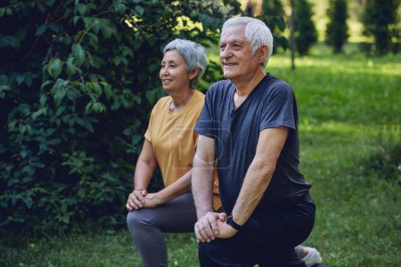 Photo for Senior spouses doing sportive exercises outdoor in summer park in the morning. Hoary healthy older couple warming-up, doing squats smile enjoy active lifestyle outside - Royalty Free Image