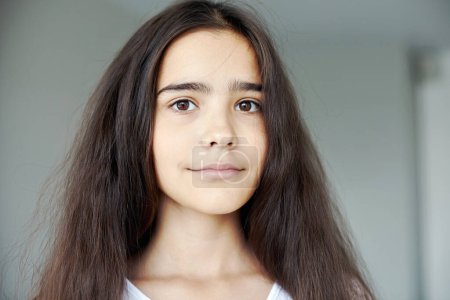 Photo for Serious beautiful preteen 12s girl pose indoors, having long brunette hair smile looking at camera. Generation Z or Alpha person portrait - Royalty Free Image