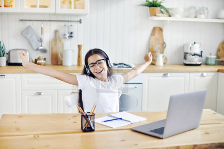 Photo for Pretty pre-teen 12s girl in headphones sit at table with laptop finish on-line class, lesson with tutor, making task, take break, relaxing with arms raised feel happy. Study, modern technologies, rest - Royalty Free Image