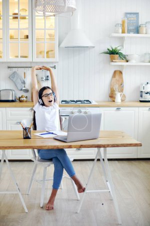 Photo for Pretty pre-teen 12s girl in headphones sit at table with laptop finish on-line class, lesson with tutor, making task, take break, relaxing with arms raised feel tired. Study, modern technologies, rest - Royalty Free Image