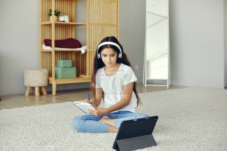 Photo for Pretty pre-teen 12s girl wear wireless headphones, sit on floor listen audio course studying, home-schooling using digital tablet. Modern tech usage for e-learning, education, gen Z new skills gaining - Royalty Free Image