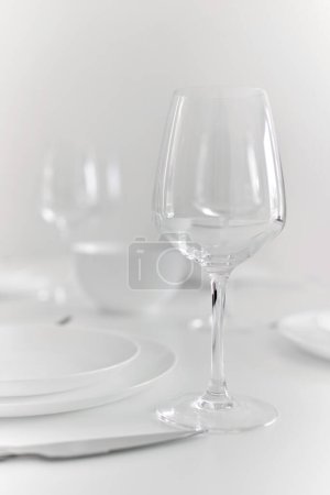 Photo for Close up view of empty wine glass on table prepared for dinner with tablecloth and plates, no people. Eating, life event celebration - Royalty Free Image