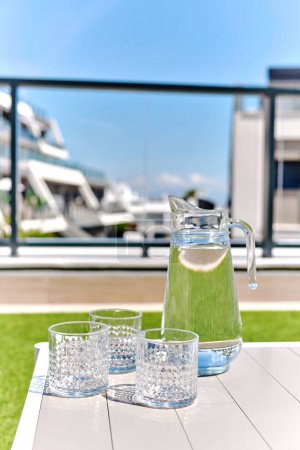 Téléchargez les photos : Gros plan de la cruche avec de l'eau douce naturelle et des verres propres vides sur une table en terrasse d'été, personne. Rafraîchissements d'été, mode de vie sain, pour prévenir la déshydratation concept - en image libre de droit