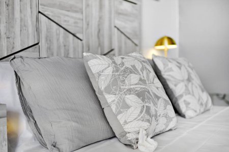 Téléchargez les photos : Gros plan des coussins gris sur le lit dans une chambre confortable éclairée par une lampe de chevet - en image libre de droit