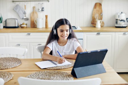 Photo for Pretty pre-teen 12s girl in wireless headphones sit at table e-learning, listen on-line course, audio lesson, receive new knowledge, skills using internet and modern tech. Child development. Education - Royalty Free Image
