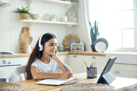 Photo for Pretty pre-teen 12s girl in wireless headphones sit at table e-learning, listen on-line course, audio lesson, receive new knowledge, skills using internet and modern tech. Child development. Education - Royalty Free Image