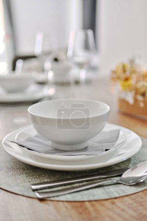 Close up white porcelain tableware plates on place mats and empty wine glasses ready for dinner. Table settings wait for guests at home or restaurant. No peopl