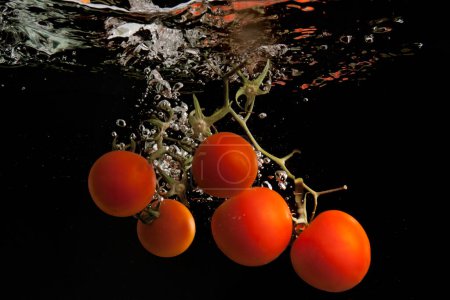 Tomaten unter Wasser erzeugen einen dynamischen Spritzeffekt mit Blasen und Wellen vor schwarzem Hintergrund.