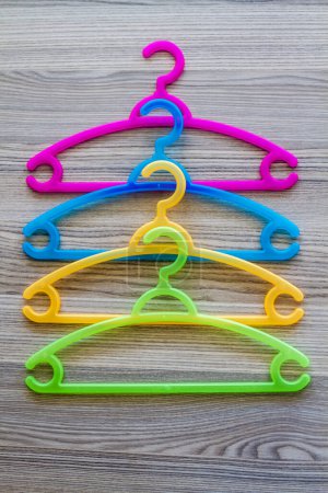 Téléchargez les photos : Empilement de quatre cintres en plastique coloré, violet, bleu, vert, jaune, sur fond de bois gris. - en image libre de droit