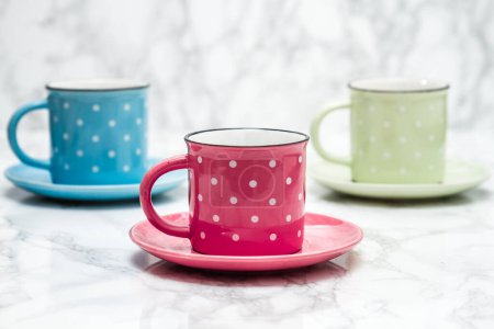 Colorful ceramic mugs, pink, blue and yellow with white dots.