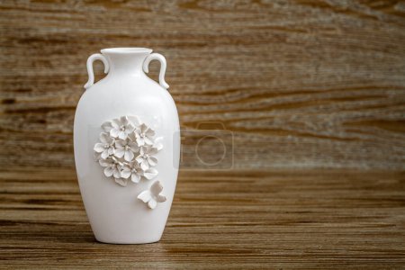 Vase blanc décoratif avec des dessins complexes sur fond en bois.