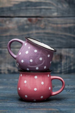 Photo for Ceramic mugs in pink and purple with white dots on wooden table. - Royalty Free Image