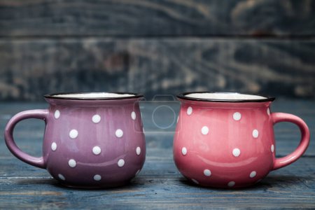 Photo for Pink and purple ceramic mug with white dots on blue wooden background. - Royalty Free Image