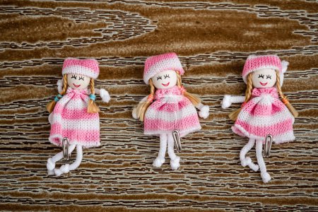 Decorative doll hangers in pink dresses on brown wooden background.