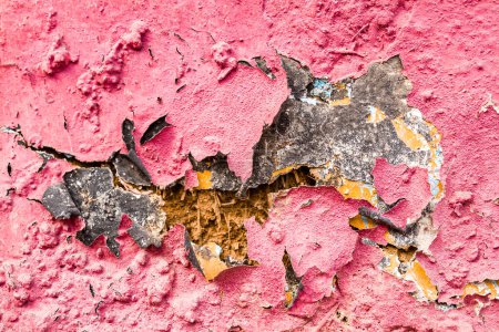 Alte rissige Lehmziegelwand mit abgeblättertem rosa Putz, ein Zeugnis von Zeit und Struktur.