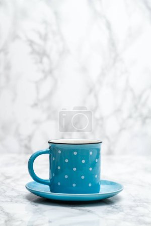 Blue ceramic mug with white dots on marble.
