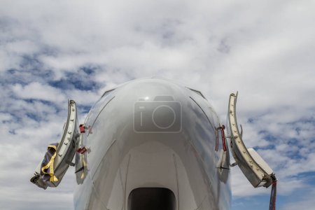 Close up view of the front of an airplane with open cockpit doors against a cloudy sky.