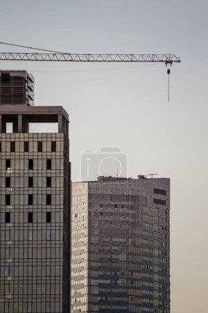 Photo for Large construction crane towering over two tall buildings against a clear sky, indicating ongoing construction. - Royalty Free Image