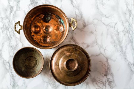 Photo for Three round copper pots placed on a marble surface with intricate gray veining. One with ornate handles, another with copper lids. - Royalty Free Image