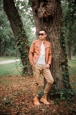 Téléchargez les photos : Un jeune homme beau se tient sous un arbre dans un parc d'automne - en image libre de droit
