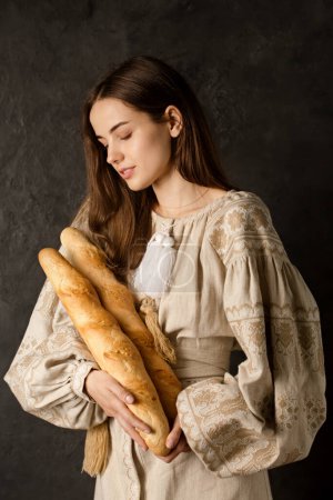 Photo for A Ukrainian woman in national clothes holds crispy baguettes in her hands - Royalty Free Image
