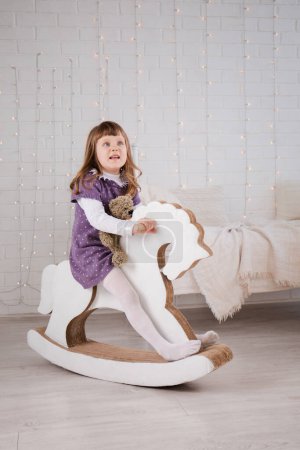 A little girl rides on a toy cardboard horse in the children's room