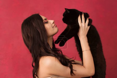 Hermosa mujer sosteniendo un gato negro sobre un fondo rosa.