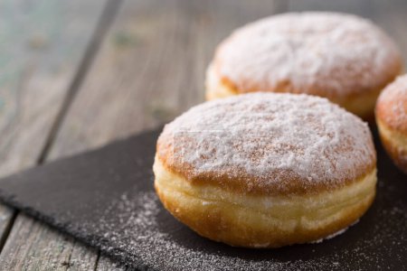 Ruddy delicious donuts berliners with filling sprinkled with powdered sugar on a rustic background