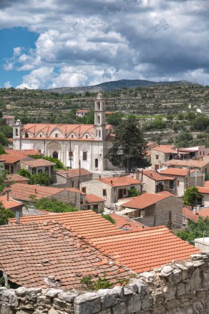 Vista panorámica de un pintoresco pueblo de Lofou con iglesia arquitectónica y techos de terracota contra un cielo nublado. Distrito de Limassol, Chipre