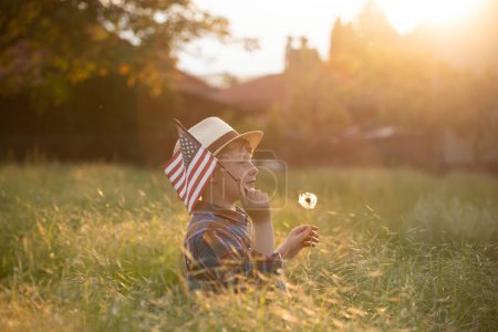 Cute little child girl with American flag in sunset field. USA celebrate 4th of July.